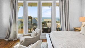 A bedroom with a large bed, a chair, and a view of a building through large windows. - Summer Wind 7 Bedroom Home by RedAwning (Santa Rosa Beach)