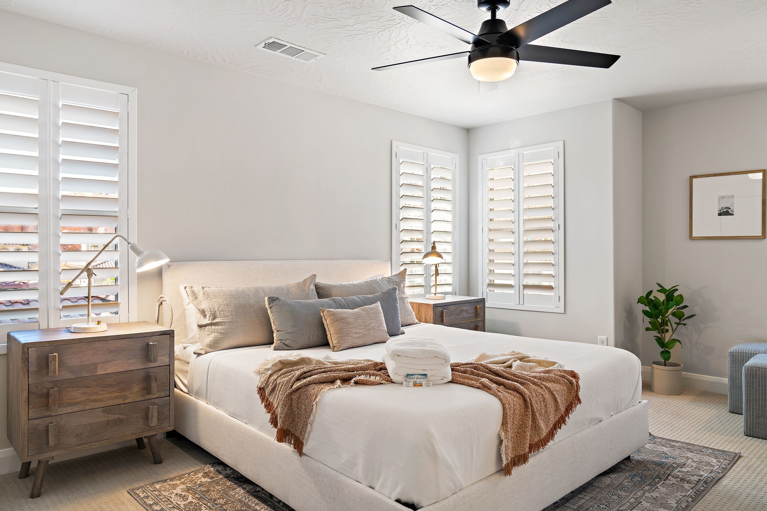 A bedroom with a bed, nightstands, a ceiling fan, and a potted plant.