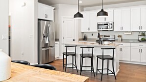 A modern kitchen with white cabinets, stainless steel appliances, and black bar stools.