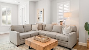 A modern living room with a sectional sofa, a wooden coffee table, and a large window with white shutters.