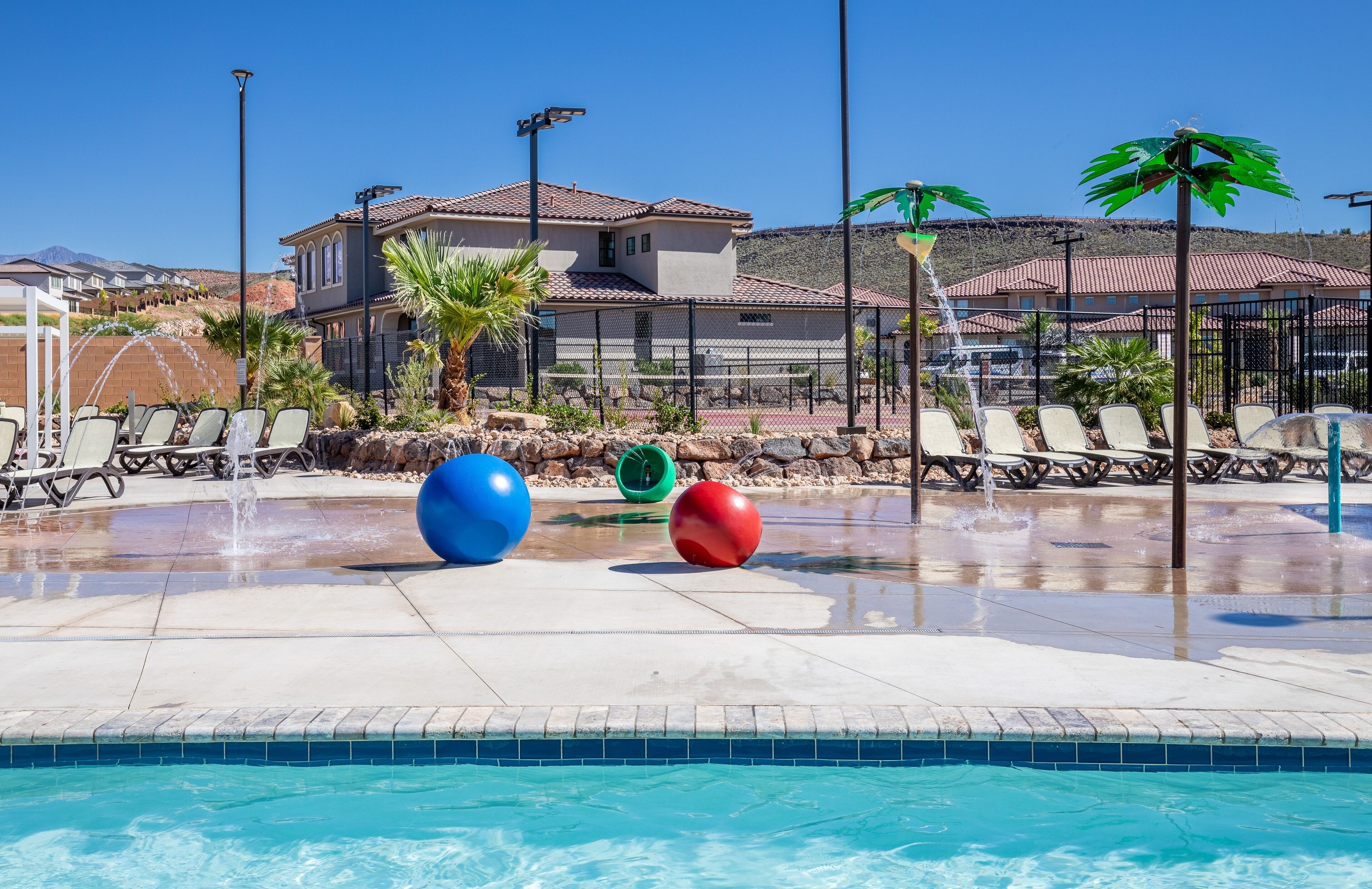 A pool area with lounge chairs, a water feature, and a building in the background.