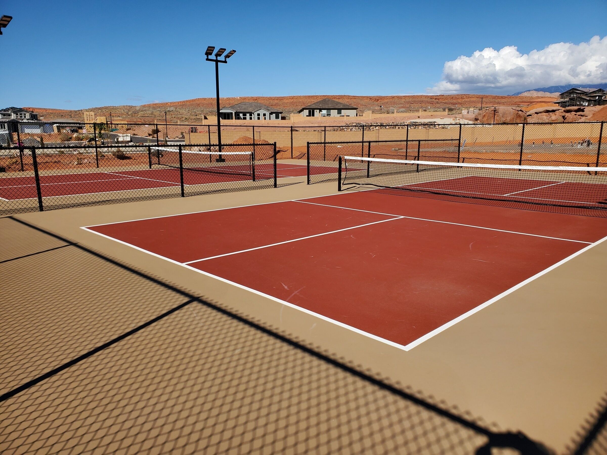 A tennis court with a net, surrounded by a fence, and buildings in the background.