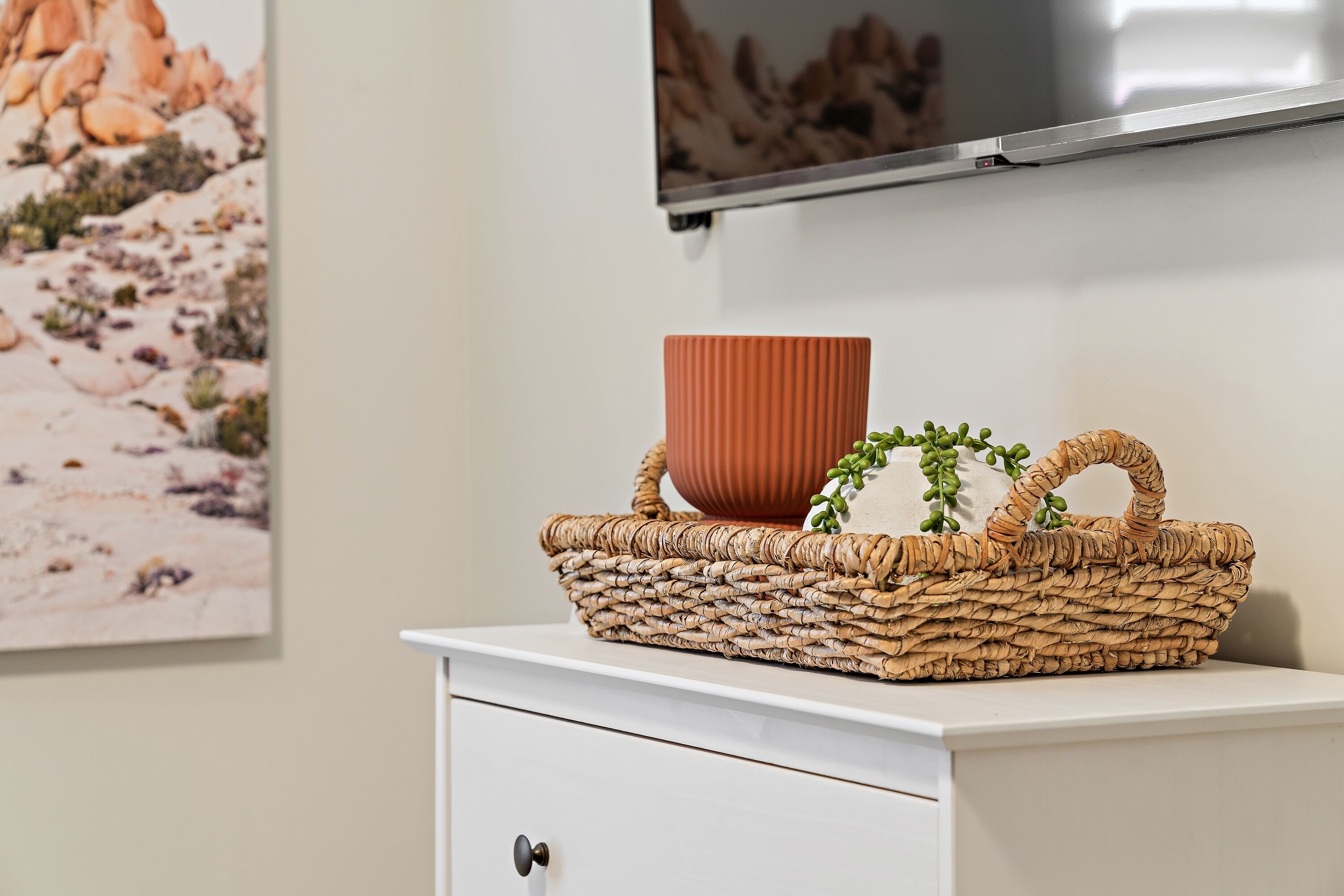 Un mueble blanco con una cesta tejida que contiene una maceta marrón y plantas verdes.
