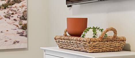 Un mueble blanco con una cesta tejida que contiene una maceta marrón y plantas verdes.