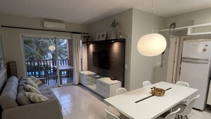 A modern living room with a sofa, dining table, and chairs. There is a kitchen area with a refrigerator and a dining table. - Apartment inside a beachfront hotel (Aquiraz)