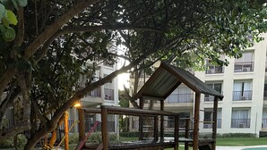 A playground with a wooden slide and climbing structure, surrounded by a paved area and a building in the background. - Apartment inside a beachfront hotel (Aquiraz)