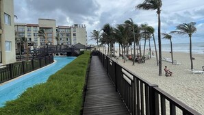 A wooden boardwalk leading to a beach with palm trees and a pool. - Apartment inside a beachfront hotel (Aquiraz)