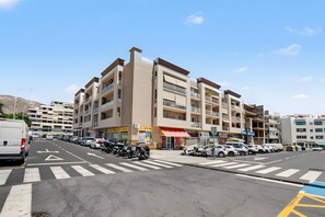 Ein mehrstöckiges Gebäude mit Geschäftsflächen im Erdgeschoss, einem Parkplatz und blauem Himmel.