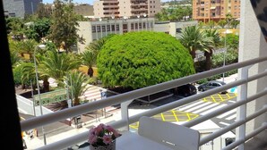 Un balcón con vista a un estacionamiento, un árbol verde y edificios al fondo.