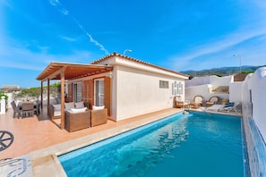 A poolside area with a covered seating area, a pool, and a view of the surrounding landscape.
