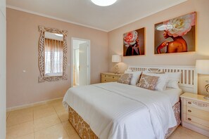 A bedroom with a bed, nightstands, a mirror, and two paintings on the wall.