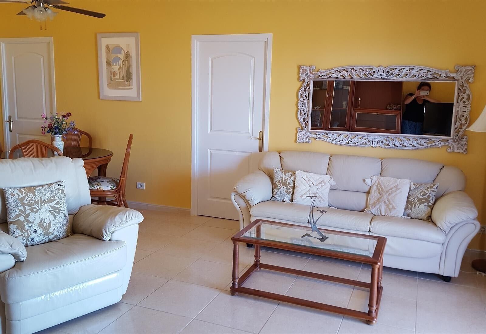 A living room with a sofa, armchair, coffee table, and a decorative mirror.