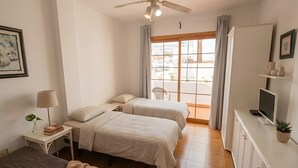 Un dormitorio con dos camas, un escritorio, una silla, un televisor y una ventana con cortinas.