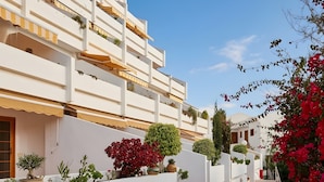 Un edificio blanco con balcones, un paseo de baldosas y plantas en macetas.