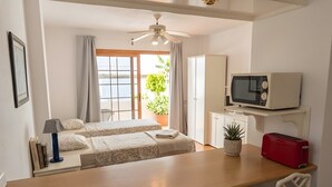 Una habitación con cama, un escritorio con sillas, microondas, tostadora y ventilador de techo.