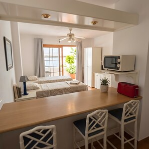 A room with a bed, a desk with chairs, a microwave, a toaster, and a ceiling fan. - Studio Apartment in central area of Las Americas. (Playa de las Américas)