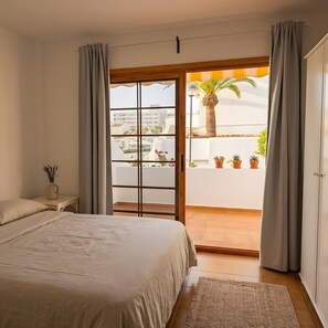 A bedroom with a bed, a nightstand, a window with curtains, and a view of the outside balcony. - Studio Apartment in central area of Las Americas. (Playa de las Américas)