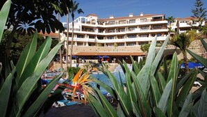 Et resort med pool, palmer og en flerlænget bygning med altaner.