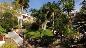Et resort med en velholdt have, palmer og en stentrappe, der fører op til en bygning.