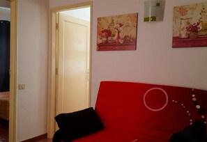 Un canapé rouge avec des coussins noirs, une porte donnant sur une autre pièce et deux tableaux accrochés au mur.