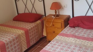 Une chambre avec deux lits simples, une table de chevet avec une lampe et une commode.
