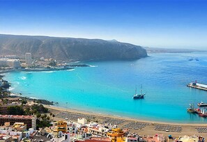 A coastal town with a beach, boats, and a large mountain in the background.