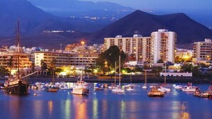 Un port de plaisance avec des bateaux, un grand immeuble et une montagne en arrière-plan.