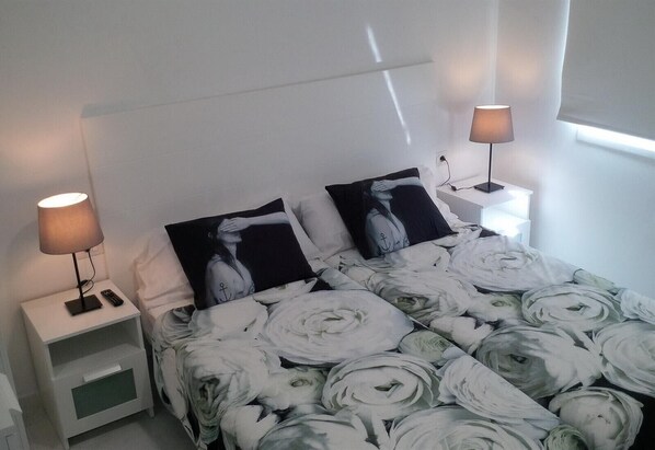 A neatly made bed with a floral bedspread, two bedside lamps, and two pillows with a black and white design.