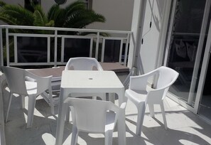 A balcony with white plastic chairs and a table, a glass door, and a white railing.