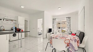 Une cuisine moderne avec un coin repas, des meubles blancs et un sol carrelé.