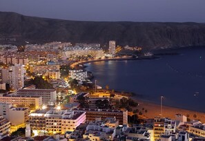 A coastal cityscape with buildings along the waterfront, a prominent hotel with a large balcony, and a mountain in the background. - Holiday Accommodation "Nice stay in Plaza Los Cristianos centre"  (Los Cristianos)