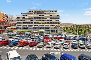 A multi-story parking structure with cars parked in designated spaces, surrounded by buildings and palm trees.