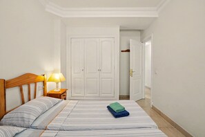 Une chambre à coucher comprenant un lit, une table de chevet avec une lampe, une armoire et une porte donnant sur une autre pièce.