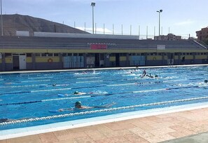 Une piscine avec des couloirs de nage, une zone réservée aux spectateurs et un bâtiment portant une enseigne.