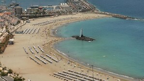 An aerial view of a coastal area with a beach, a lighthouse, and a marina with boats.