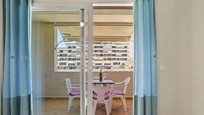 A balcony with a table and chairs, a view of a building, and a window with curtains.