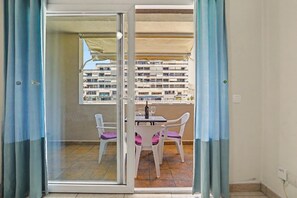 Een balkon met een tafel en stoelen, uitzicht op een gebouw, en een raam met gordijnen.