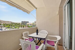 Un balcon avec une table et des chaises, une bouteille de vin et une vue sur un paysage urbain avec des immeubles et des palmiers.