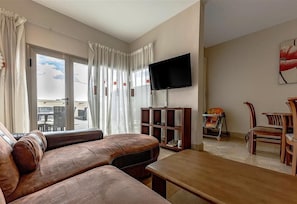 Una sala de estar con sofá, televisor, mesa de madera y comedor con sillas.
