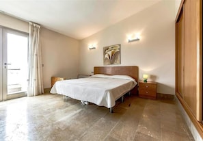 Un dormitorio con cama, mesita de noche, lámpara, un cuadro y una puerta corrediza.