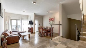 Uma sala de estar ampla com sofá, mesa de jantar e cadeiras, escada e televisão sobre um armário.