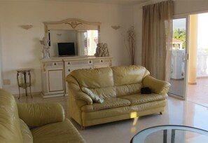 A living room with a beige sofa, a television on a cabinet, and a glass table.