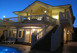 Una casa de dos pisos con un balcón, una piscina y una escalera que lleva a la entrada.