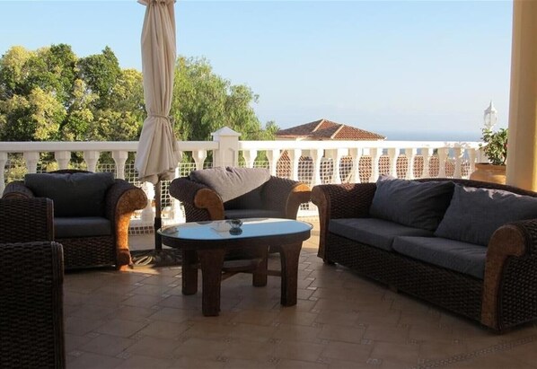 Un patio con mobiliario de mimbre, una mesa de vidrio y vista al mar.