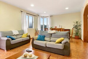 A living room with two grey sofas, a wooden coffee table, and a dining table with chairs. - Holiday Home 'Vinháticos House' with Mountain View, Garden & Wi-Fi (São Vicente)