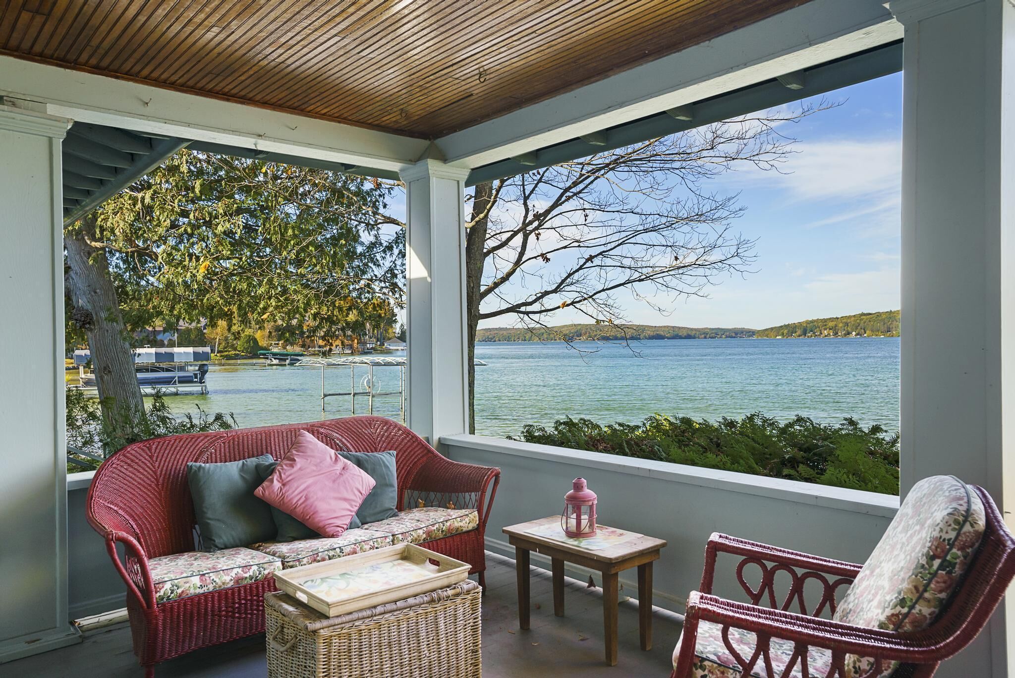 Ein überdachter Balkon mit Korbmöbeln, Blick auf einen See und einen Baum.