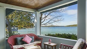 A covered balcony with wicker furniture, a view of a lake, and a tree. - Classic Walloon Lake Cottage (Boyne City)
