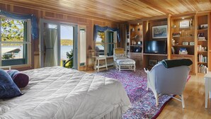 A bedroom with a large bed, a chair, a TV, and a bookshelf. - Classic Walloon Lake Cottage (Boyne City)