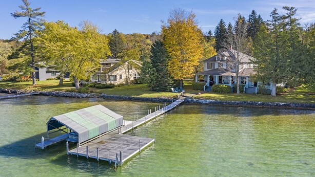A lakeside property with a dock, a covered boat house, and houses surrounded by trees. - Classic Walloon Lake Cottage (Boyne City)