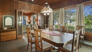 A dining area with a wooden table and chairs, a chandelier, and large windows with curtains. - Classic Walloon Lake Cottage (Boyne City)